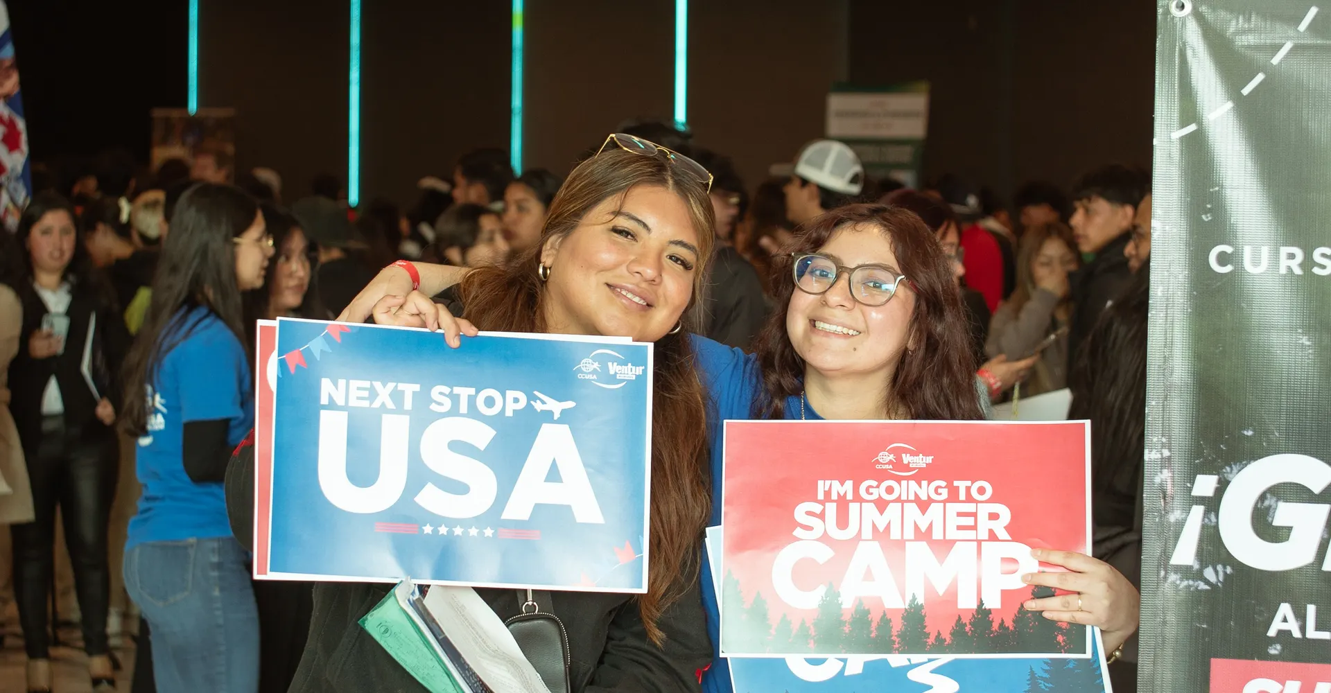 Participantes en la feria sosteniendo carteles de «Next Stop USA» e «I'm going to Summer Camp»