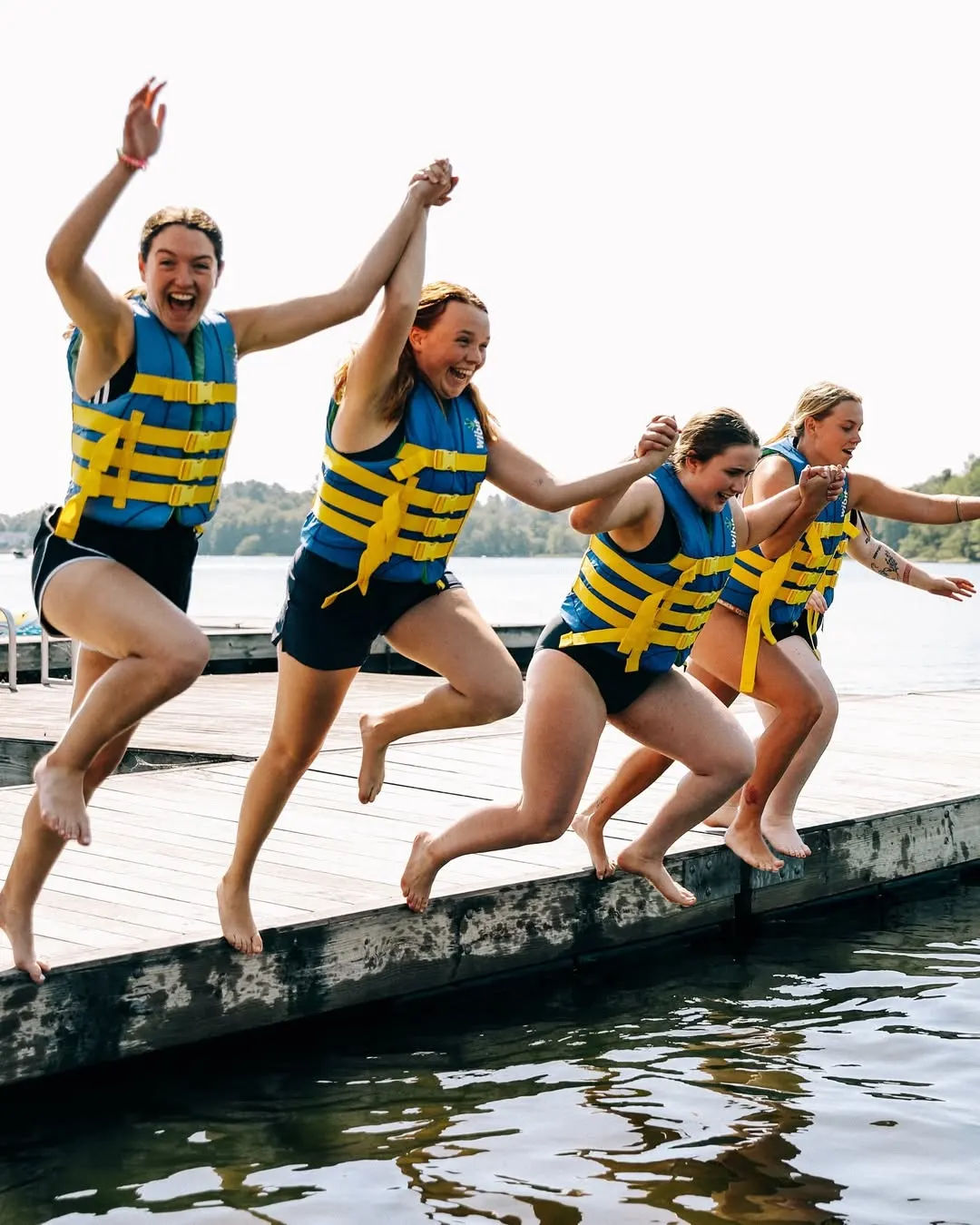 Grupo de participantes con chalecos saltando al lago desde el muelle